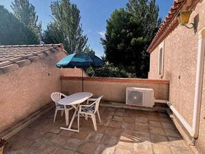 A patio with a table and chairs, an air conditioning unit, and a blue umbrella. - Calm apartment near the beach - 2 guests (Bouzigues)