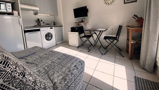 A compact living space with a kitchenette, a washing machine, a dining area with a table and chairs, a bed, and a television. - Calm apartment near the beach - 2 guests (Bouzigues)