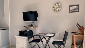 A compact kitchenette with a flat-screen TV, a small table, two chairs, and a wooden shelf above the counter. - Calm apartment near the beach - 2 guests (Bouzigues)