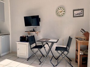 A compact kitchenette with a flat-screen TV, a small table, two chairs, and a wooden shelf above the counter. - Calm apartment near the beach - 2 guests (Bouzigues)