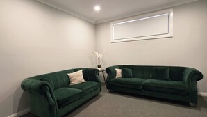 Ein Zimmer mit zwei grünen Sofas, einem kleinen Tisch mit Blumenvase und einem gerahmten Bild an der Wand.