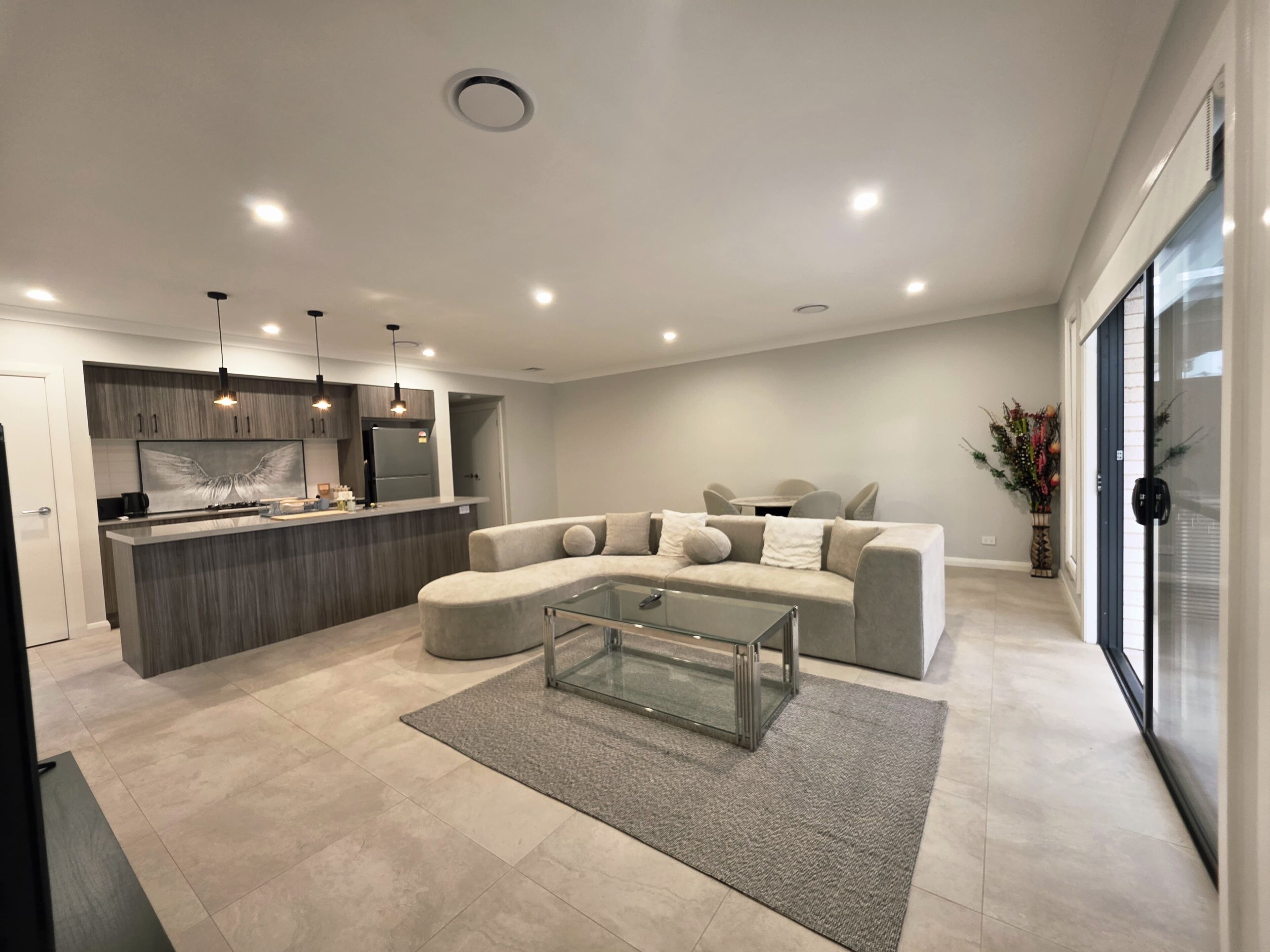 Una sala de estar moderna con un sofá seccional, una mesa de centro de vidrio y una zona de cocina con isla integrada.