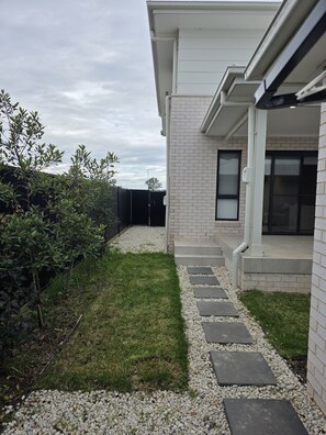 A modern house with a paved driveway, a small lawn, and a gravel pathway leading to the entrance. - Modern 4BR House w/ All Queen Beds & Private Master Ensuite (Oran Park)