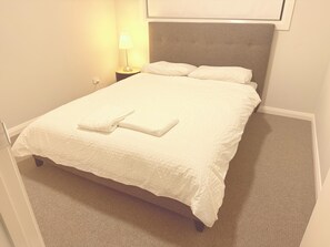 A neatly made bed with a folded towel, a bedside lamp, and a headboard. - Modern 4BR House w/ All Queen Beds & Private Master Ensuite (Oran Park)