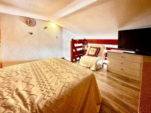 Ein Schlafzimmer mit einem Bett, einem Schminktisch, einem Fernseher und einem roten Kopfteil.