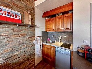 A compact kitchen with a dishwasher, wooden cabinets, a stone backsplash, and a hanging towel rack. - Comfortable duplex studio - 4 guests (Crest-Voland)
