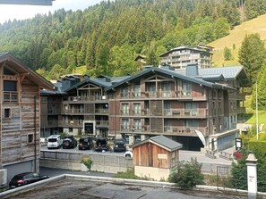 A multi-story hotel with balconies, a parking area, and a view of a forested hillside. - Central apartment with parking - 4 guests (Les Gets)
