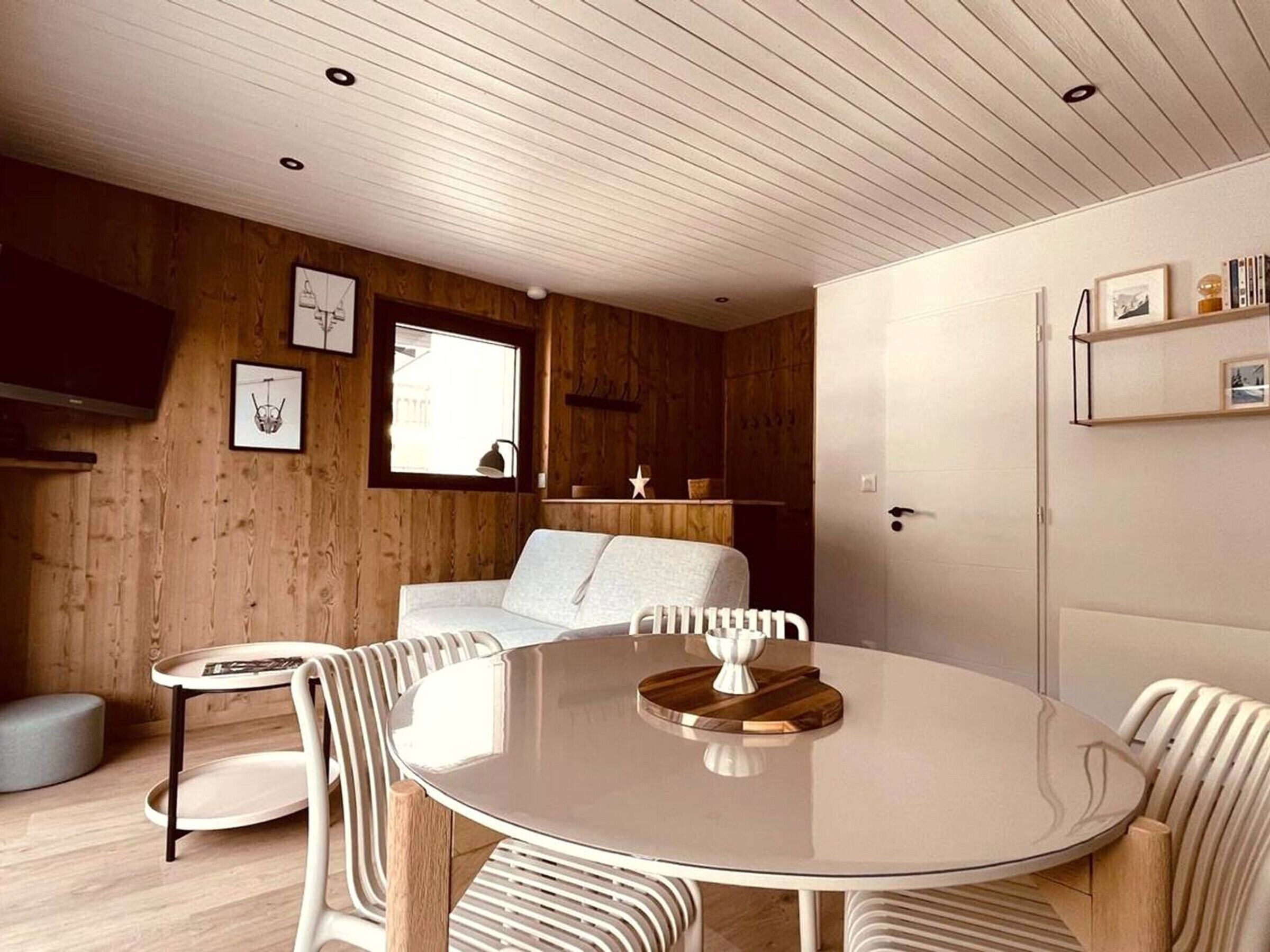 A modern interior with a round dining table, white chairs, a sofa, and a wooden wall.