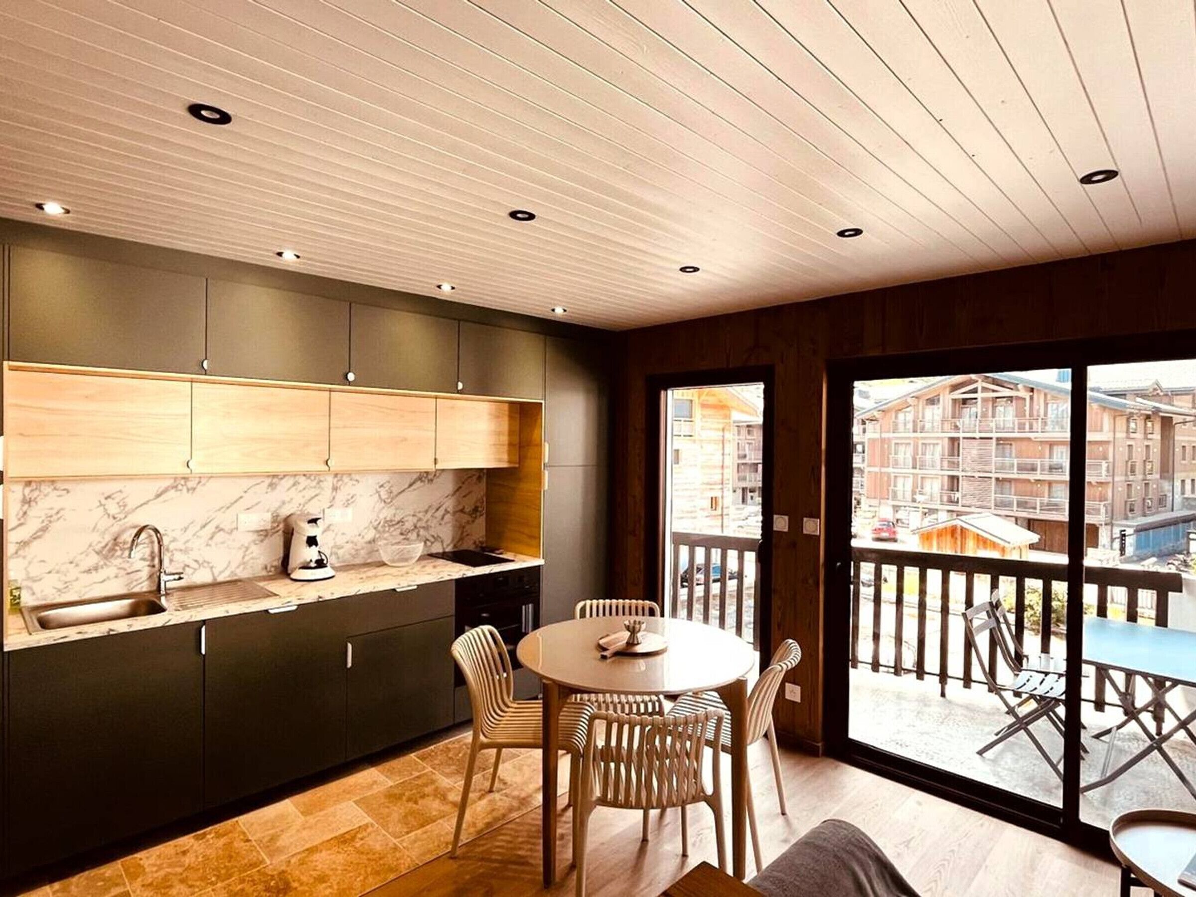 A modern kitchen with a marble countertop, wooden cabinets, and a dining area with a round table and chairs.