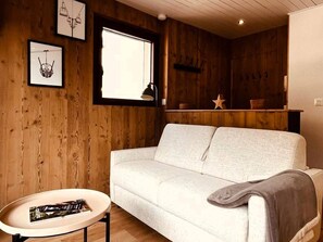 Ein gemütliches Zimmer mit einer weißen Couch, einem kleinen runden Tisch und Holzwänden.