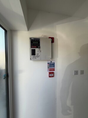 A fire alarm control panel mounted on a wall, a fire action sign, and a red emergency pull station. - House Sleeps 9 With Wifi (Slough)