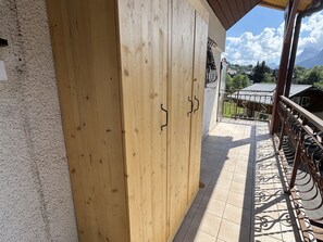 Uma porta de madeira com maçaneta de metal, que dá para uma varanda com piso de azulejos e grade de ferro forjado.