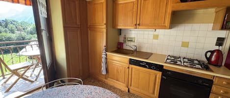 Une cuisine avec des meubles en bois, une cuisinière à gaz, un lave-vaisselle et une vue sur l’extérieur.