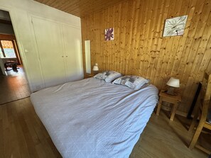 Ein Schlafzimmer mit einem großen Bett, Holzwänden, einer Tür und einem Nachttisch mit Lampe.