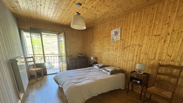 Ein Zimmer mit Holzwänden und einem Bett mit weißer Bettdecke. Ein Fenster bietet Blick auf Grünflächen.