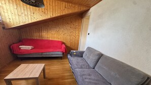 Ein Zimmer mit Holzboden, einem grauen Sofa, einer roten Decke auf einer grauen Couch und einem Holztisch.