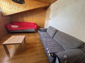 Um quarto com teto de madeira, um sofá cinzento, um cobertor vermelho sobre um sofá cinza e uma mesa de madeira.
