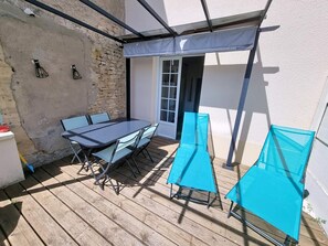A patio with a table and chairs, a covered area, and a door leading to an interior space. - Apartment near the sea - 4 guests (Saint-Aubin-sur-Mer)