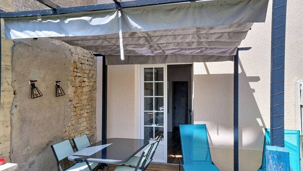 Eine Terrasse im Freien mit einem Glastisch und Stühlen, einer überdachten Sitzgelegenheit und einer Steinwand.