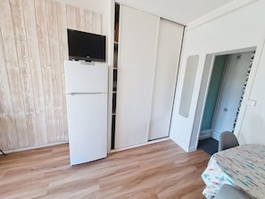 A room with a white wardrobe, a flat-screen TV mounted above it, and a dining table with a patterned tablecloth. - Apartment near the sea - 4 guests (Saint-Aubin-sur-Mer)