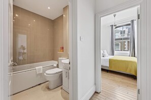 A modern bathroom with a bathtub, toilet, and sink. - 2-bed by Natural History Museum - Lift - Sleeps 6 (London)