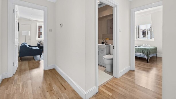 Eine moderne Wohnung mit Holzboden, einem sichtbaren Wohnbereich mit einer Couch, einem Badezimmer mit Toilette und Waschbecken sowie einem Schlafzimmer mit einem Bett.
