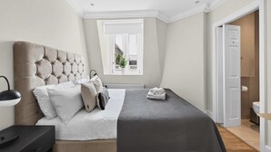 Ein Schlafzimmer mit einer gesteppten Kopfteil, einem Bett mit weißen Leinen, einer grauen Decke und einer Nachttischlampe.