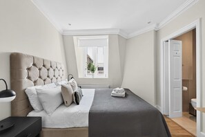 Ein Schlafzimmer mit einer gesteppten Kopfteil, einem Bett mit weißen Leinen, einer grauen Decke und einer Nachttischlampe.