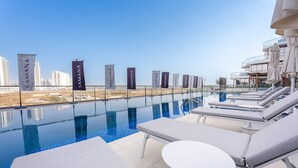 A rooftop infinity pool with lounge chairs and a view of the city skyline. - Stayshort - Gorgeous Studio Apartment in Studio City Sleeps 4 With Balcony (Dubai)
