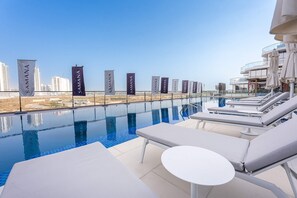A rooftop infinity pool with lounge chairs and a view of the city skyline. - Stayshort - Gorgeous Studio Apartment in Studio City Sleeps 4 With Balcony (Dubai)