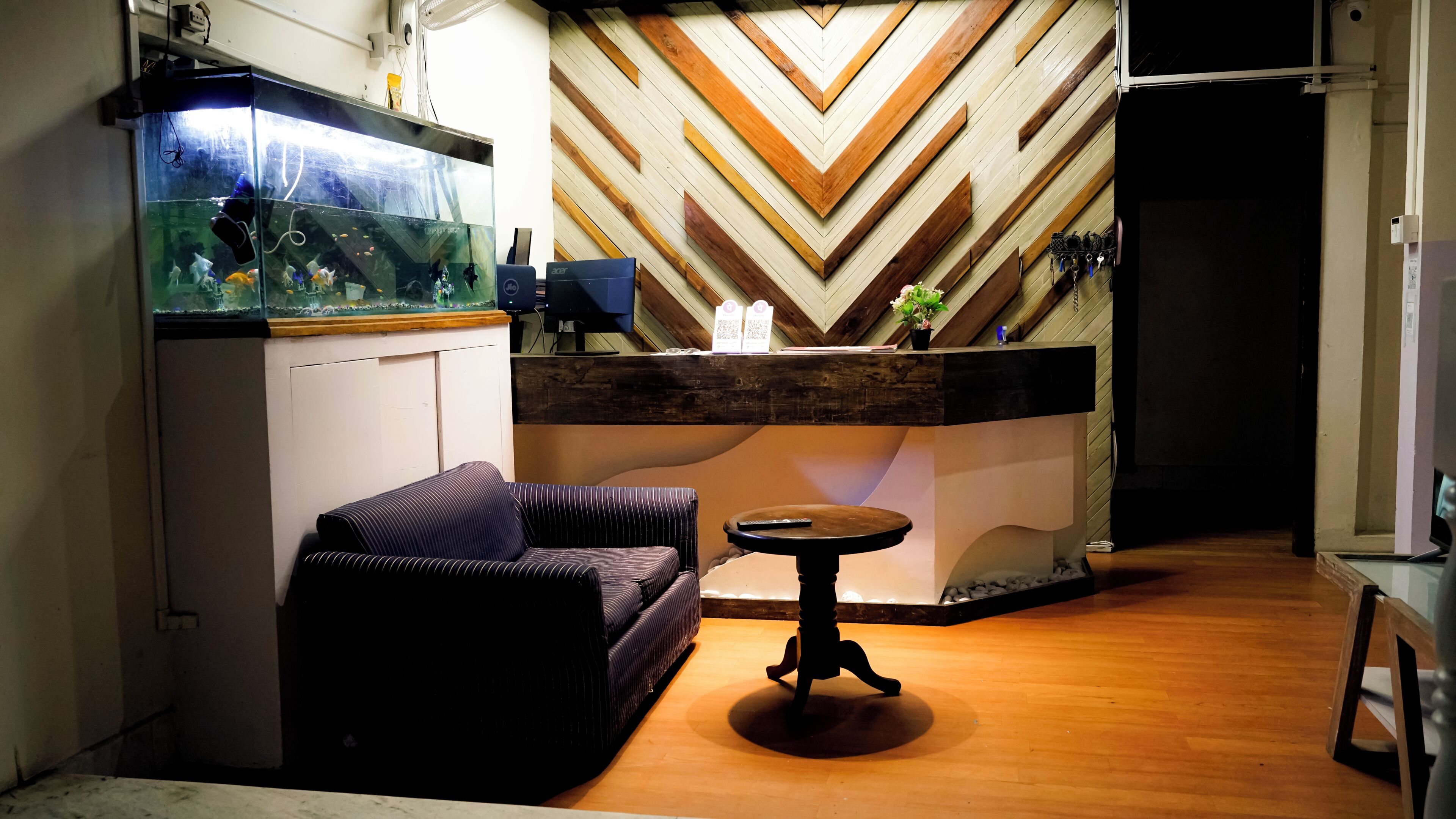 A room with a wooden floor, a sofa, a small round table, a fish tank, and a chevron-patterned wall.