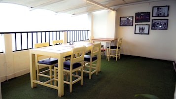 Um quarto com uma mesa e cadeiras de madeira, uma pequena mesa com um laptop e quadros nas paredes.