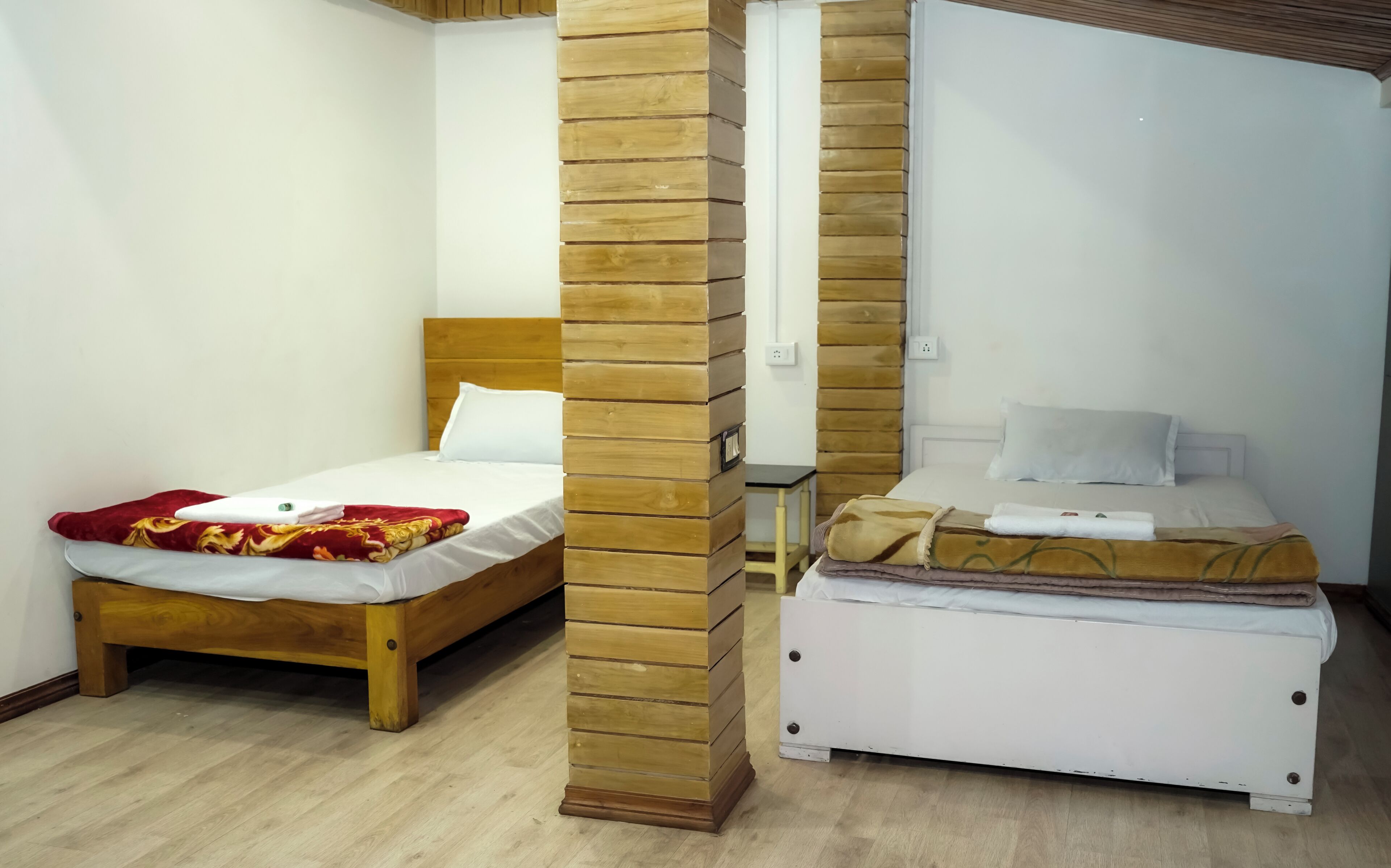 Una habitación con dos camas, una con cabecera de madera y la otra con cabecera blanca. Hay una mesita entre las camas.