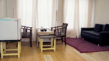 A compact living space with a dining table, two chairs, a black sofa, a red rug, and a white refrigerator.