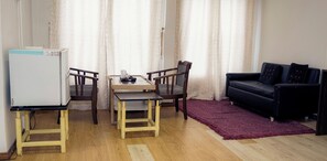 A compact living space with a dining table, two chairs, a black sofa, a red rug, and a white refrigerator. - The Mystic Hill Hotel-Aizawl Mizoram (Aizawl)