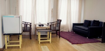 Espaço compacto com mesa de jantar, duas cadeiras, sofá preto, tapete vermelho e geladeira branca.