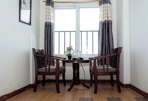 A dining area with a table and two chairs, a window with curtains, and a framed picture on the wall. - The Mystic Hill Hotel-Aizawl Mizoram (Aizawl)