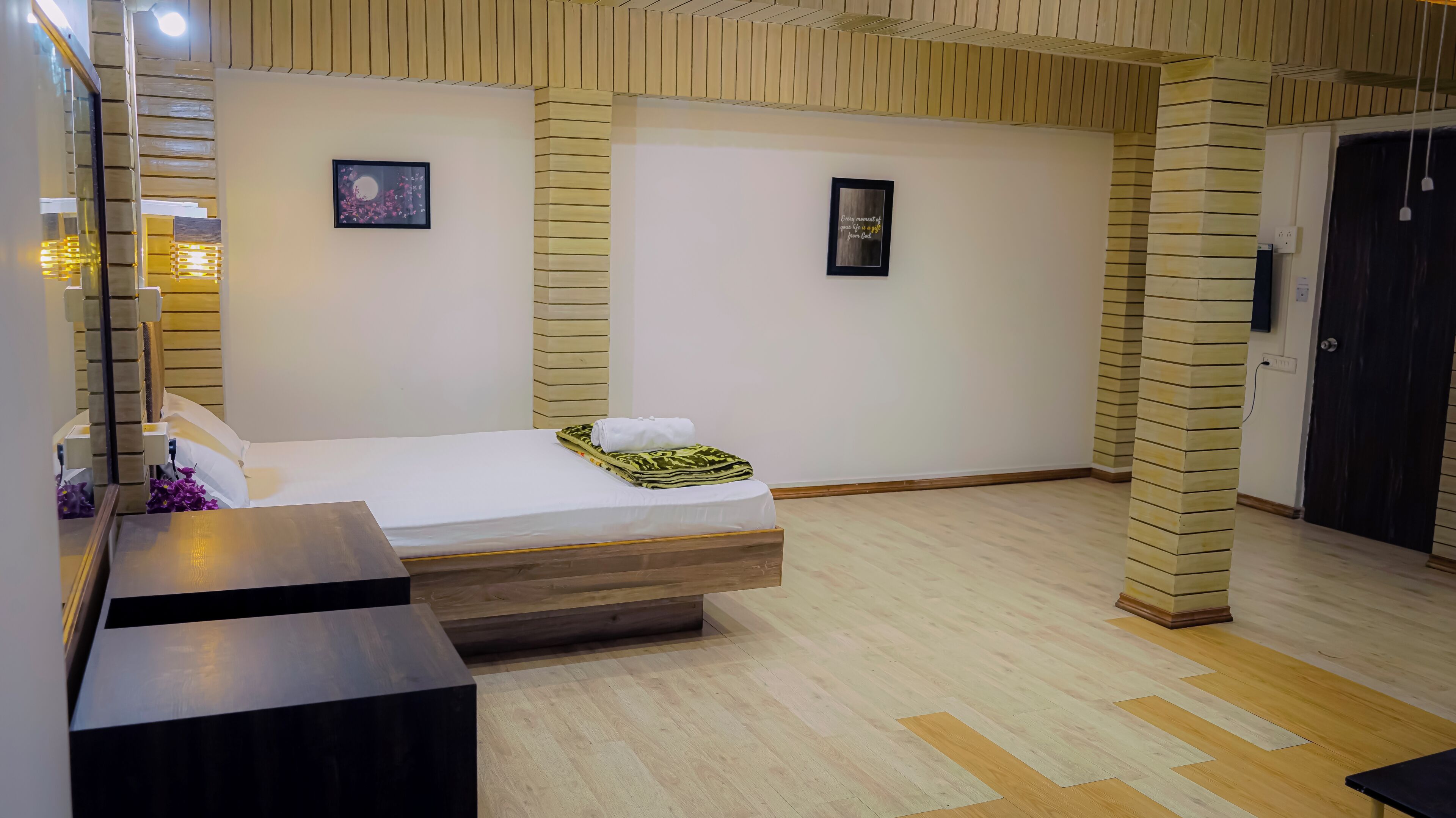A hotel room with a bed, a bedside table, a mirror, and a wall-mounted picture.