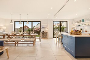 A modern kitchen with a large island, dining area with wooden furniture, and large windows offering a view of the backyard. - Duneside House - North East Escapes (Beadnell)