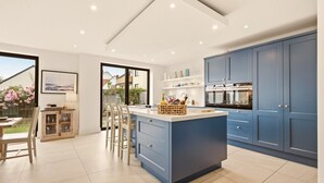 A modern kitchen with a central island, blue cabinets, and a view of the outdoors. - Duneside House - North East Escapes (Beadnell)
