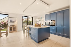 A modern kitchen with a central island, blue cabinets, and a view of the outdoors. - Duneside House - North East Escapes (Beadnell)