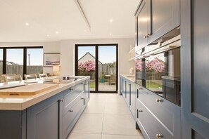 A modern kitchen with a large island, built-in appliances, and a sliding glass door leading to a backyard. - Duneside House - North East Escapes (Beadnell)