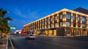 A modern hotel with a large entrance, a well-lit facade, and a clear sky.