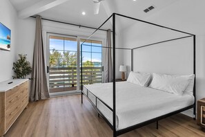 Een moderne slaapkamer met een hemelbed, een schuifdeur naar een balkon en een houten dressoir.