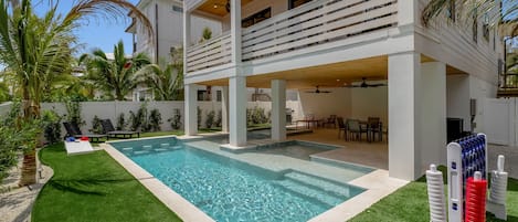 A modern two-story house with a swimming pool, outdoor seating, and palm trees.
