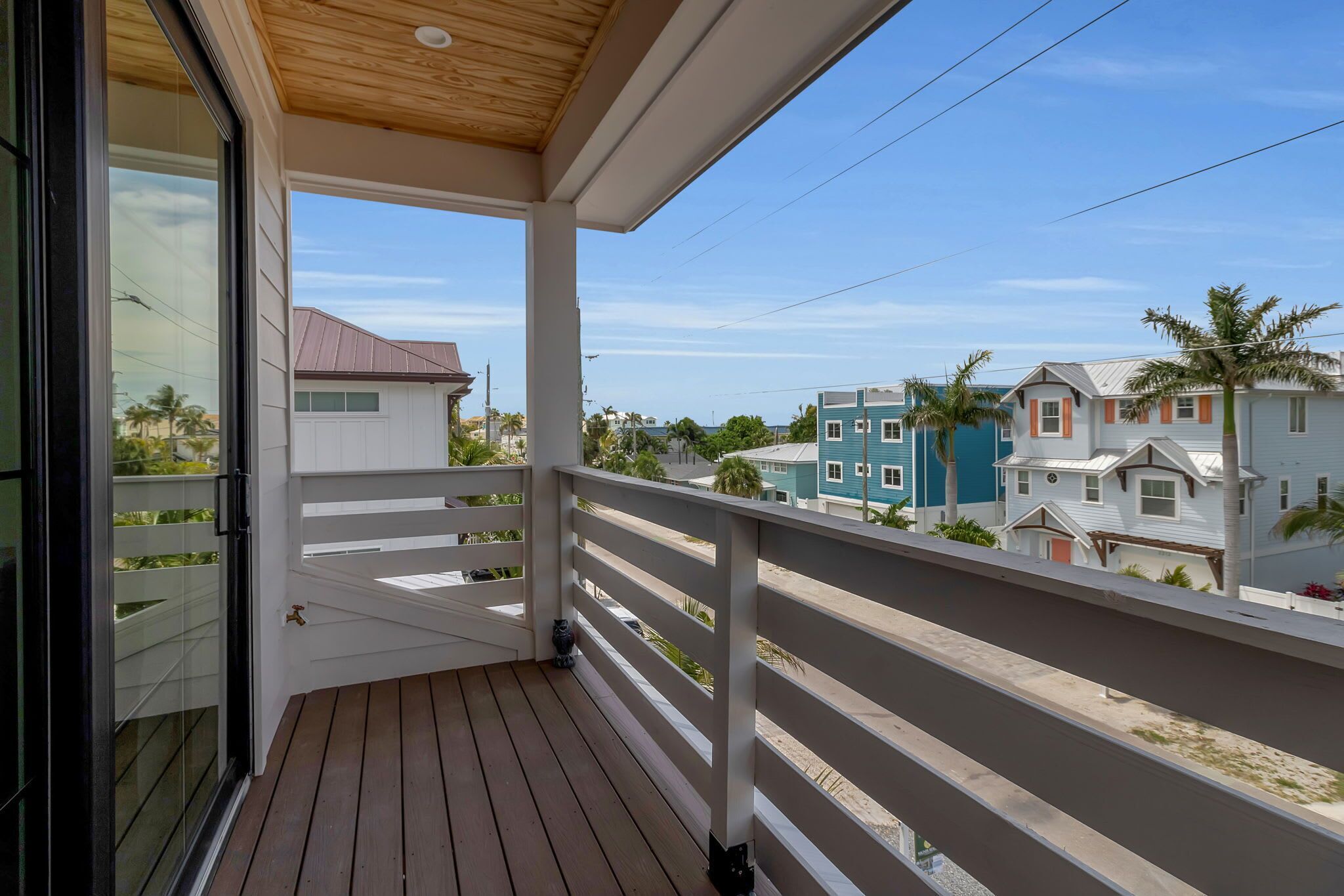 Uma varanda com piso de madeira, grades brancas e vista para casas vizinhas.