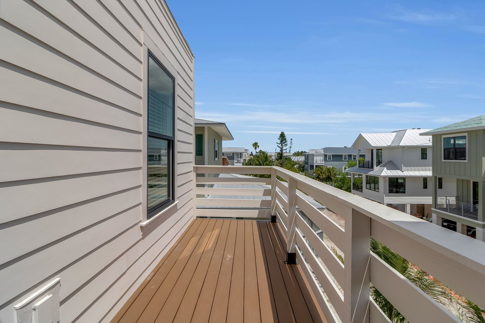 A residential deck with a white railing, a large window, and a view of neighboring houses.