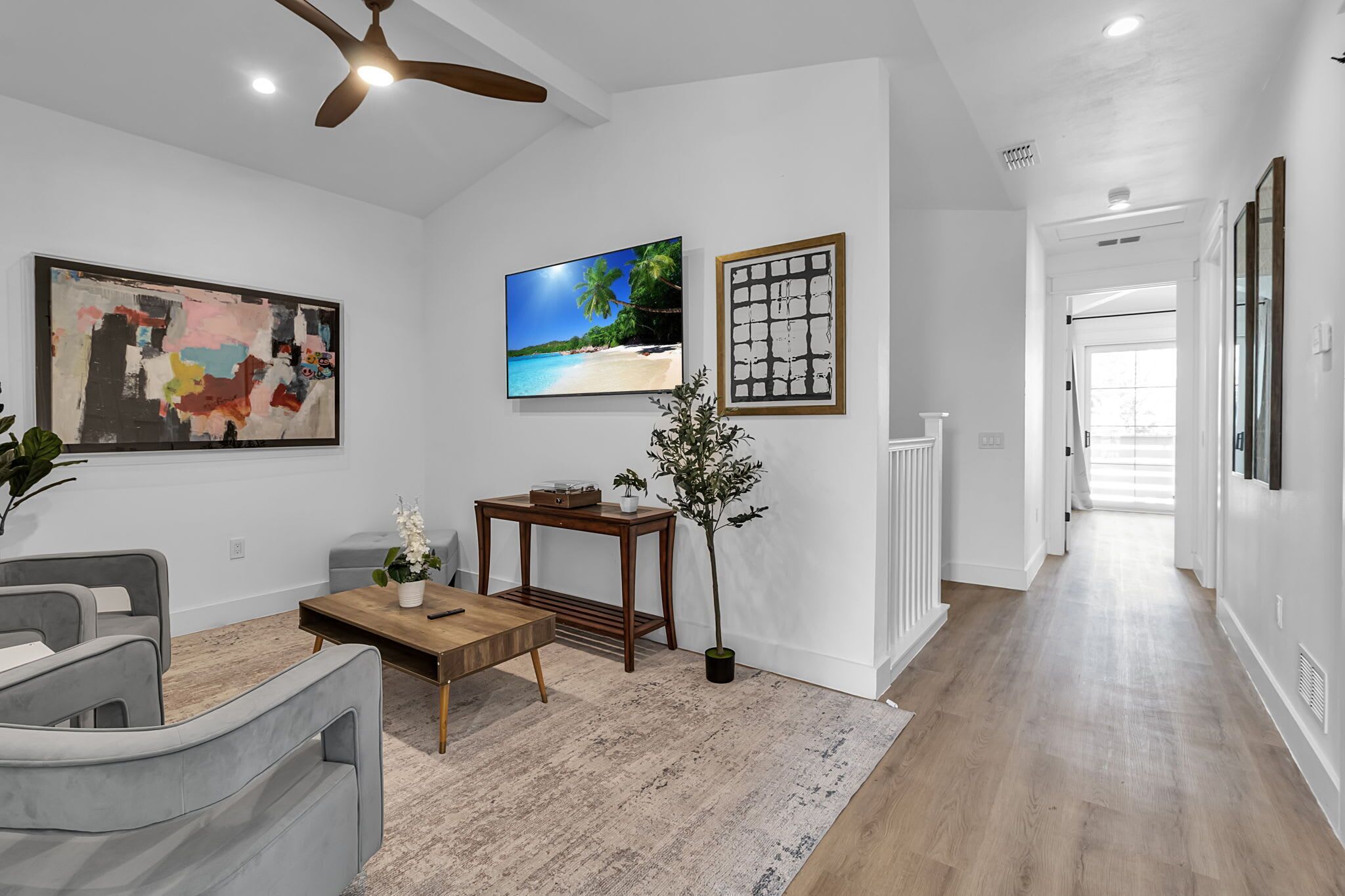 A modern living room with a sofa, coffee table, TV, artwork, and a plant.