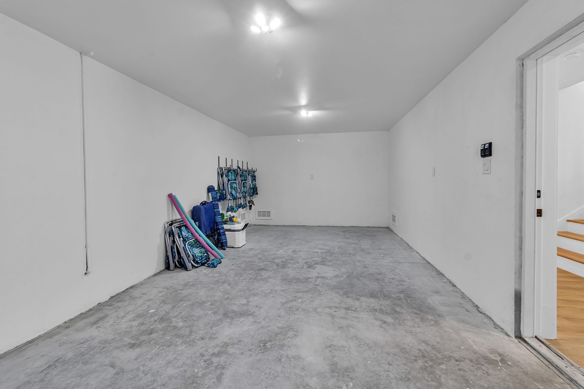 A spacious, empty room with white walls, a concrete floor, and a door leading to a wooden staircase.