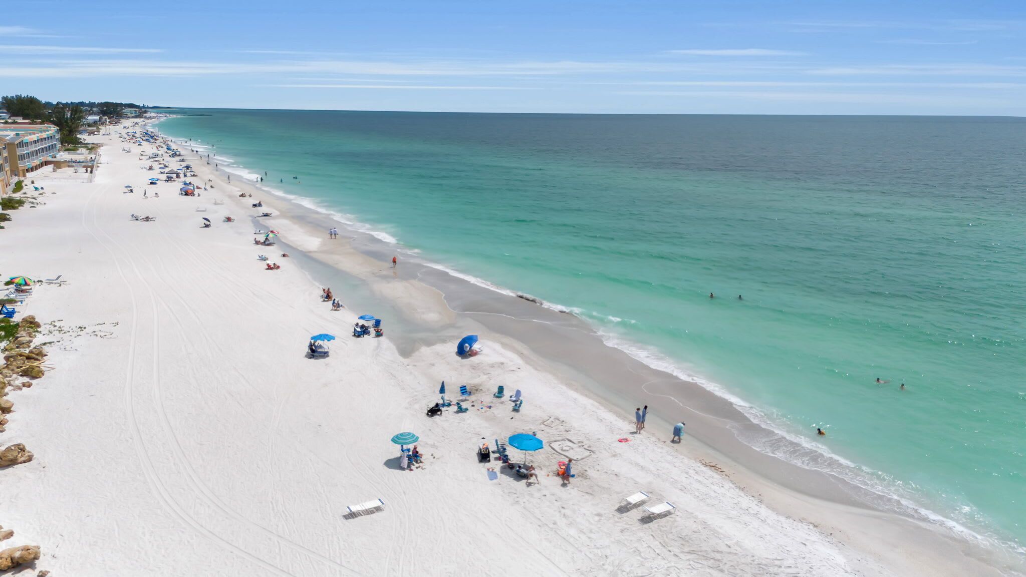 Une plage avec une eau turquoise et limpide, une longue étendue de sable, ainsi que plusieurs parasols et chaises de plage.